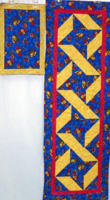 Christmas table runner (no placemats)gold and blue cotton prints, machine pieced by Margaret Sudbey and machine quilted by Linda Monasky.    <br />